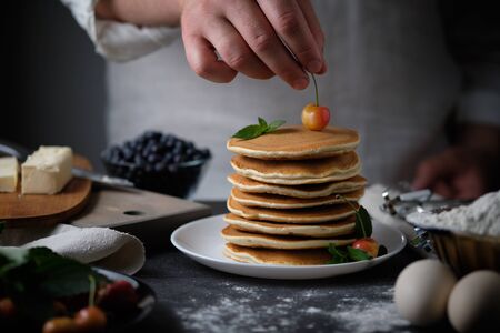 Father cooks pancakes for breakfast. Cook in the process of cooking pancakes. Pancakes with berries. The hands of man in the frame.の写真素材