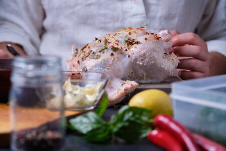 A man rubs chicken with a mixture of pepper, lemon and herbs. The process of cooking chicken in the oven. On the table are the products that are needed for cooking. The hands of the cook in the frame.の写真素材