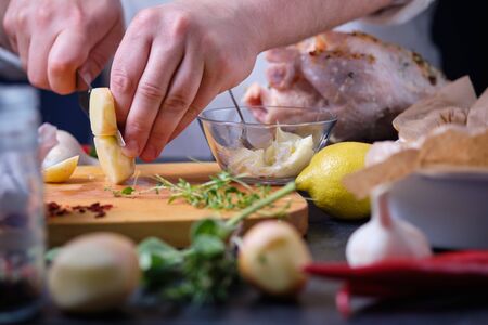A man cuts a young potato. The process of cooking chicken with herbs, spices and lemon in the oven. On the table are the products that are needed for cooking. The hands of the cook in the frame.の写真素材
