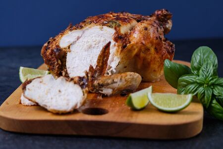 Sliced pieces of oven baked chicken with spices, herbs and lemon on a wooden board with a beautiful ruddy crust.の写真素材