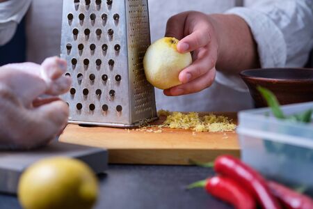 Man rubs lemon zest. The process of cooking chicken with herbs, spices and lemon in the oven. On the table are the products that are needed for cooking. The hands of the cook in the frame.の写真素材