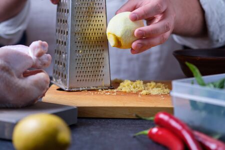 Man rubs lemon zest. The process of cooking chicken with herbs, spices and lemon in the oven. On the table are the products that are needed for cooking. The hands of the cook in the frame.の写真素材