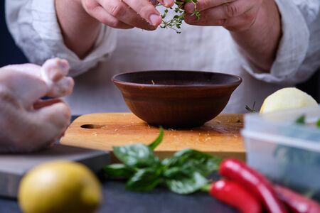 Man puts thyme in a plate. The process of cooking chicken with herbs, spices and lemon in the oven. On the table are the products that are needed for cooking. The hands of the cook in the frame.の写真素材