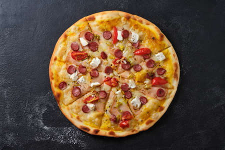 Pizza with tomatoes, ham, onions, feta cheese, mozzarella cheese, spicy sausages, spices and mustard sauce. Flat lay. On a dark background.の写真素材