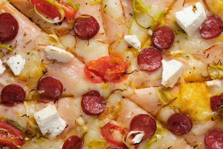 Pizza with tomatoes, ham, onions, feta cheese, mozzarella cheese, spicy sausages, spices and mustard sauce. A closeup of a pizza.の写真素材