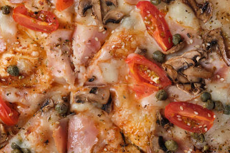 Pizza with tomatoes, ham, capers, mushrooms, mozzarella cheese, spices, sesame seeds and tomato sauce. A closeup of a pizza.の写真素材