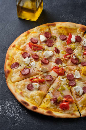 Pizza with tomatoes, ham, onions, feta cheese, mozzarella cheese, spicy sausages, spices and mustard sauce. On a dark background.の写真素材