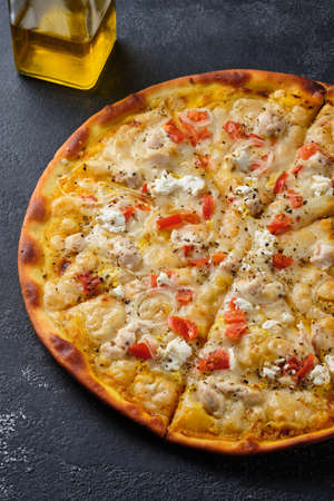 Pizza with tomatoes, chicken, onions, feta cheese, mozzarella cheese and spices. On a dark background.の写真素材