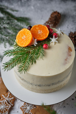 Delicious New Year's cake with poppy sponge cake and tangerine filling. A beautiful holiday cake for Christmas decorated with tangerines, fresh berries, snowflakes and spruce twigs.の写真素材