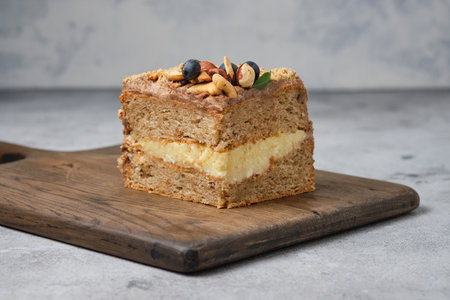 Piece of cake with cream and nuts on a wooden cutting board