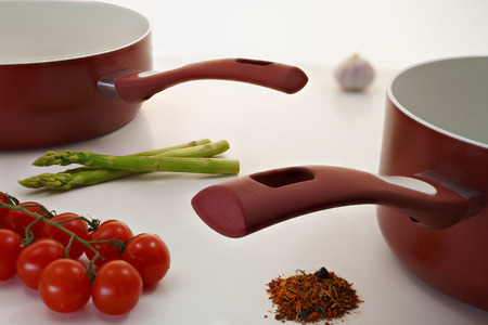 Two Burgundy saucepan with vegetables on a white table の写真素材
