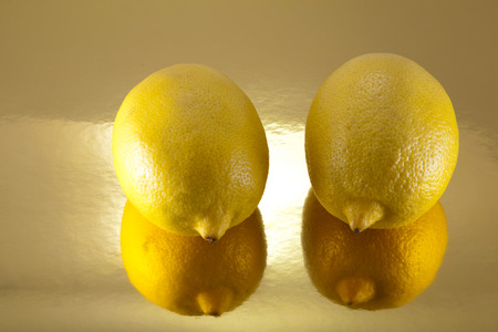 two lemons on a golden background with reflectionsの写真素材