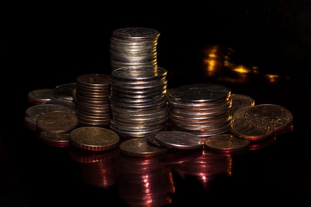 small coins against a dark background with shadows and color patches of lightの写真素材
