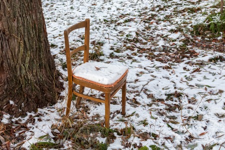 The brown chair forgotten outdoors at a tree under a snow layerの写真素材