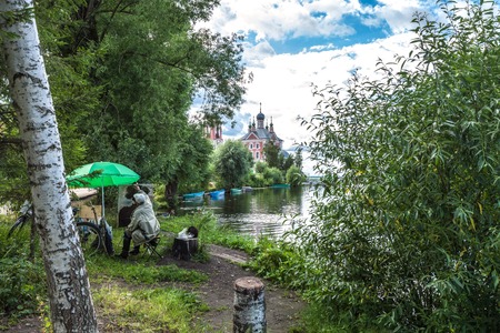 Pereslavl Zalessky, Russia - July 21, 2016: The unknown painter in leather boots and with a black cat on hemp draws an imperceptible tree on other river bank though directly before him a wonderful landscape.のeditorial素材