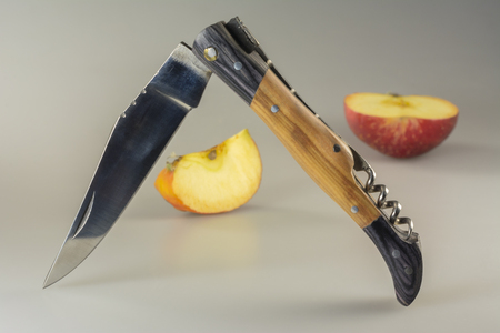 Folding tourist knife and half-cut apple on a gray tableの写真素材