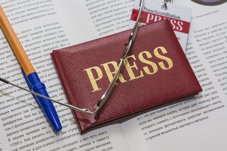 Operating license PRESS, PRESS badge, sunglasses, a pen and an open magazine on the tableの写真素材