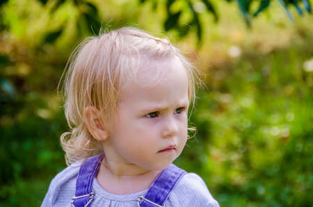 Little girl in blue denim overalls, summer at the cottage in the gardenの写真素材
