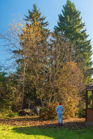 A woman in a gray sports suit and a red hat looks at the autumn forest near the porch of the houseの写真素材