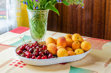 Ripe sweet cherry and apricots on a table in a vaseの写真素材