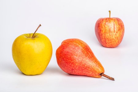 Yellow and red apples and a red pear on a table on a white backgroundの写真素材