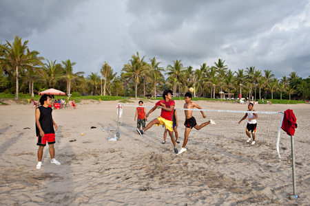 Indonesia, Kuta, February 25, 2010 ,Young people on the beach play a ball legs through a grid.のeditorial素材