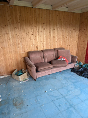 A neglected living room with a worn-out sofa and scattered debris on a blue tiled floorの写真素材