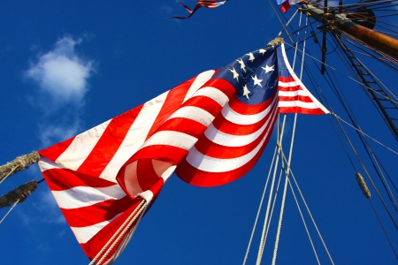 United States flag blows in the wind on the mast of a tall sailing ship 