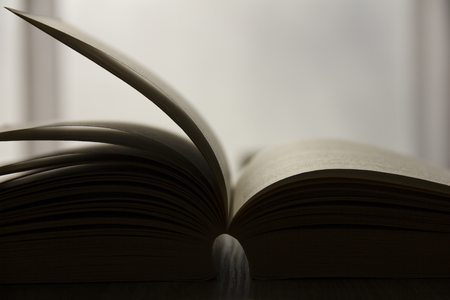 Closeup of an open book on a wooden table with a bright backgroundの写真素材