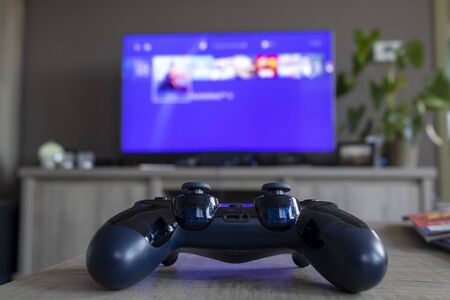 A portrait of a PlayStation 4 controller, which is turned on, directly facing a television, which is displaying the PlayStation home screen.のeditorial素材