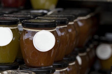 A close up portrait of a row of stacked glass pots with a metal black lid on top, and a label around them. They contain jam or jelly in a fruit or mixed fruit flavour.の写真素材