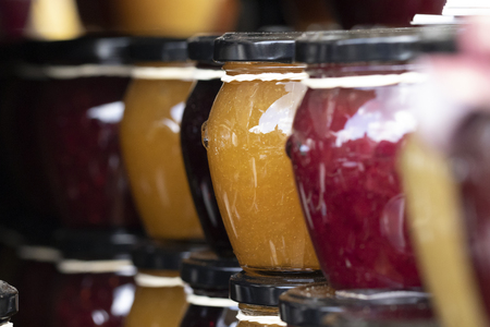 A close up portrait of rows of stacked glass pots with a metal black lid on them, with colorfull contents. The content is jam in different fruit or mixed fruit flavours.の写真素材