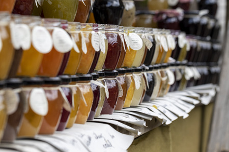 BEERVELDE, BELGIUM - MAY 12 2019: A close up portrait of glass pots with portions of different kinds of jam in them displayed on a market stall at a local market. All kinds of fruit and mixed fruit flavours and colors are available in glass pots with a meのeditorial素材