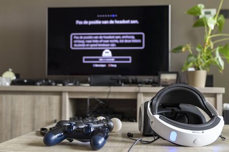 BRECHT,BELGIUM - JUNE 29 2019: A portrait of a playstation controller, a playstation virtual reality headset and move controllers on a table. In the background there is a blurred television.のeditorial素材