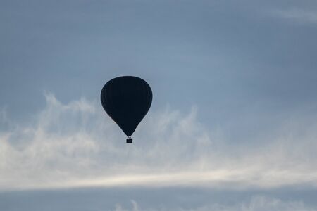 A portrait of a hot air balloon silhouette in a blue sky with some clouds on a sunny day.の写真素材