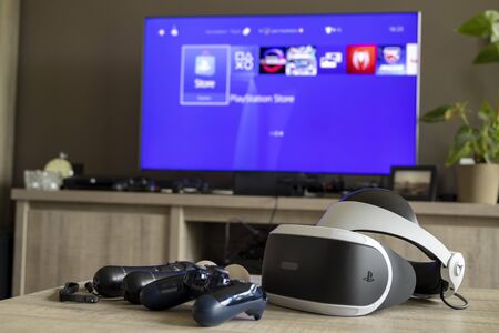 Brecht, Antwerp, Belgium - June 6 2019: A shot of some playstation 4 controllers with the playstation VR headset in front of a tv displaying the playstation home screen.のeditorial素材