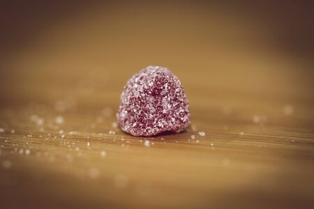 A macro portrait of a small piece of red candy sprinkled with sugar on a wooden table.の写真素材