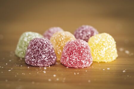 A close up portrait of soms colorful sugar sprinkled pieces of cany. The sweets are placed on a wooden table with sugar sprinkled around them.の写真素材