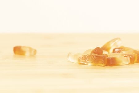 A very light and dreamy portrait of some cola bottle shaped candy on a wooden table. The sweets have the same colors as a half full bottle of cola.の写真素材