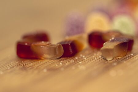 A portrait of different pieces of colorful candy lying on a wooden table with sugar sprinkled all around them. The sweets in focus are shaped like cola bottles.の写真素材