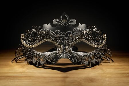 A portrait of a venetian mask on a wooden table put into the spotlight in the surrounding darkness. The perfect prop to take to a costumed ball or halloween party.の写真素材