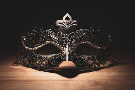 A portrait of a traditional venetian mask on a wooden surface appearing mysteriously out of the darkness.の写真素材