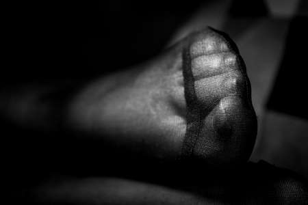 A close up black and white potrait of a girls pantyhose feet and the reinforced toe on a couch indoor.の写真素材