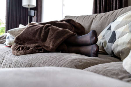 A potrait of a girls black pantyhose feet while she is sleeping in the couch in the living room under a brown cozy blanket.の写真素材