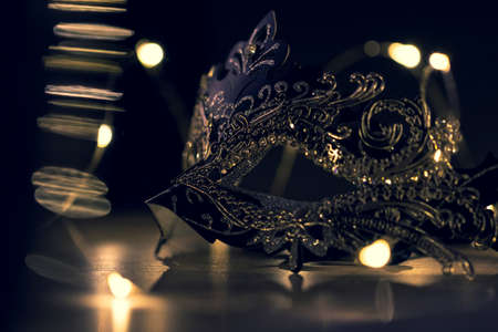 A portrait of a venetian mask on a wooden table surrounded by lights. The mask is to be worn to hide someones identity at a party like halloween.の写真素材