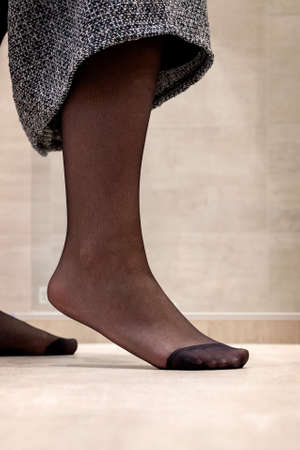 A close up portrait of a foot standing on the tip in sexy black pantyhose of a girl pulling up her skirt. The nylon is reinforced at the toes.の写真素材