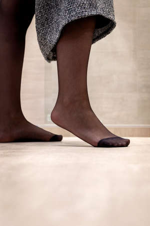 A close up portrait of a foot standing on the tip in black pantyhose of a girl pulling up her skirt. The nylon is reinforced at the toes.の写真素材