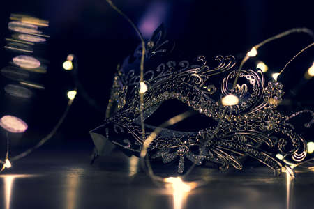 A portrait of a venetian mask in the evening full of mystery on a wooden table surrounded by lights. It is perfect to hide someones identity on a masked ball.の写真素材
