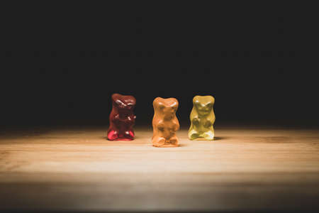 A portrait of three different colored gummy bears, the candy is standing on a wooden plank with lighting that looks like they are on a stage.の写真素材