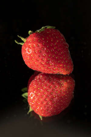 A dark portrait of a strawberry on a mirror with a nice reflection.の写真素材